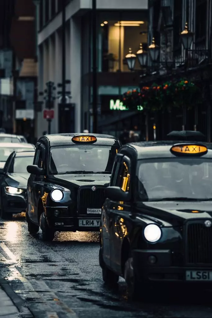 Tax Checks for PCO drivers 8 Classic London taxis navigating wet streets in an atmospheric cityscape.