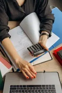 A business professional uses a calculator among documents and laptop on a desk for financial tasks.